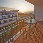 Terrasse mit Tisch und Stühlen, Blick auf Meer und Gebäude.