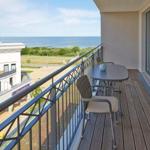 Terrasse mit Tisch und Stühlen, Blick auf Meer und Gebäude.