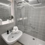 Moderne Dusche mit Duschbrause und Handbrause. Waschbecken mit Spiegel und Handtücher.