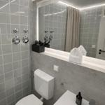 Badezimmer mit Toilette, Waschbecken und Dusche mit grauen Fliesen.