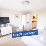 Frisch renoviertes Schlafzimmer mit Bett, TV und Blick in die Küche.