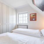 Schlafzimmer mit Bett, Kleiderschrank und Fenster.