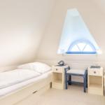 Zimmer mit zwei Betten, Schreibtisch und Dachfenster mit blauem Vorhang.