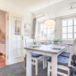Esszimmer mit Tisch, Stühlen und Fenster. Küche im Hintergrund sichtbar.