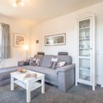 Wohnzimmer mit grauem Sofa, weißem Couchtisch und Glasvitrine.