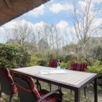 Terrasse mit Tisch und Stühlen unter strohgedecktem Dach.