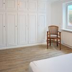 Schlafzimmer mit weißem Schrank, Holzstuhl und Blick auf Strand.