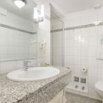 Badezimmer mit Waschbecken, Spiegel, Dusche und Toilette.