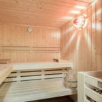 Holzsauna mit Sitzbänken, Thermometer und Eimer.