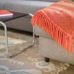Ein grauer Sessel mit orangefarbener Decke und Glas-Tisch mit rotem Buch.