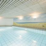 Innenpool mit Strandmotiv an der Wand und Holzdecke.