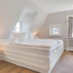 Schlafzimmer mit weißem Bett, Holzboden und Fenstern.