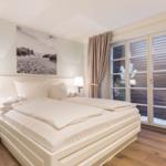 Ein Schlafzimmer mit weißem Bett, zwei Nachttischen und großen Fenstern.