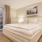 Schlafzimmer mit Doppelbett, Wandbild eines Schafs und bodentiefen Fenstern.