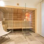 Sauna mit Glaswand, Holzbank und Fenster mit Jalousie.