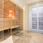 Sauna mit Holzwand und Glasabtrennung, daneben Fenster mit Jalousie.