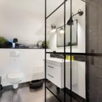 Bad mit Dusche, Waschbecken und Toilette. Schwarze Fliesen und Spiegelschrank.