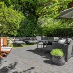 Terrasse mit Sitzgruppe, Sonnenschirm und Liegestühlen. Umgeben von Bäumen und Sträuchern.