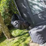 Schwarzer Hängesessel und Sitzkissen vor grauem Holzhaus mit grünem Rasen