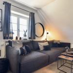 Ein Wohnzimmer mit grauem Sofa, Fenster und modernen Möbeln.