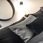 Schwarze und graue Kissen auf einem Sofa mit runden Wandspiegel und Beleuchtung.