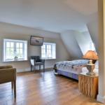 Schlafzimmer mit Bett, Fenstern, TV und Holzboden.