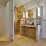 Badezimmer mit Dusche, Waschbecken und Toilette. Holzfliesen und Spiegel.