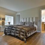Schlafzimmer mit Bett, Holzboden und Fenstern. Blick in angrenzenden Raum.