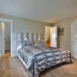 Schlafzimmer mit Bett, Holzboden und Türen zu angrenzenden Räumen.
