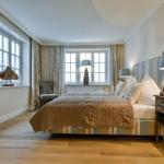 Schlafzimmer mit Bett, zwei Fenstern und Holzboden.