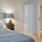 Schlafzimmer mit Bett, Nachttisch und Kleiderschrank. Tür führt in angrenzendes Zimmer.