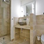 Badezimmer mit Dusche, Waschbecken und Toilette. Steinfliesen und Spiegelschrank.
