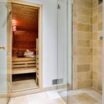 Dusche mit Glaswand und Sauna mit Holzbänken und Handtuch.