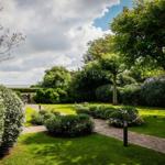 Gartenweg mit Rasen, Sträuchern und Bäumen führt zum Meer.