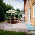 Terrasse mit Tisch, Stühlen und Sonnenschirm neben einem Haus mit Backsteinfassade.