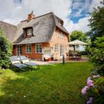 Haus mit Strohdach, Garten mit Liegestühlen und Terrasse mit Tisch.