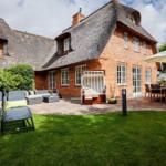Haus mit Strohdach, Terrasse, Liegestühle und Garten.