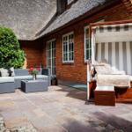 Terrasse mit Loungemöbeln und Strandkorb an Backsteinhaus mit Strohdach.