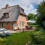 Haus mit Strohdach, Terrasse und Garten mit Liegen und Tisch.