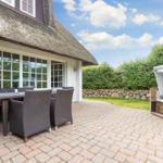 Terrasse mit Sitzgruppe und Strandkorb vor einem Haus mit Strohdach.