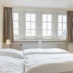 Zwei Betten unter vier Fenstern mit Vorhängen und Wandbildern.