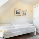 Schlafzimmer mit weißem Bett, Nachttisch und Kleiderschrank unter schräger Decke.