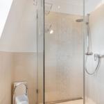 Dusche mit Glaswand, Duschbrause und Mosaikfliesen an der Wand.