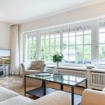 Wohnzimmer mit Sitzgelegenheiten, Fernseher und großem Fensterblick auf Garten.