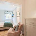 Schlafzimmer mit Bett, Sessel und Schrank. Fenster mit Rollladen und Wandbilder.
