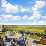Terrasse mit Tisch und Stühlen, Strandhütte und Blick aufs Meer.