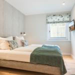 Schlafzimmer mit Bett, Fenster und Wandlampe.