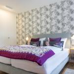 Schlafzimmer mit Bett, Nachttisch und Tapete mit Blattmuster.