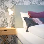 Schlafzimmer mit Bett, Nachttisch und Lampenwand mit Palmblattmuster.