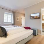 Schlafzimmer mit Bett, Fenstern und TV. Badezimmer im Anschluss.